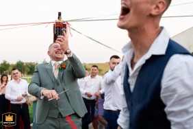 Noivo jogando o jogo da fita do buquê com uma garrafa de uísque em Oberhausbergen, França, durante uma festa de recepção de casamento.